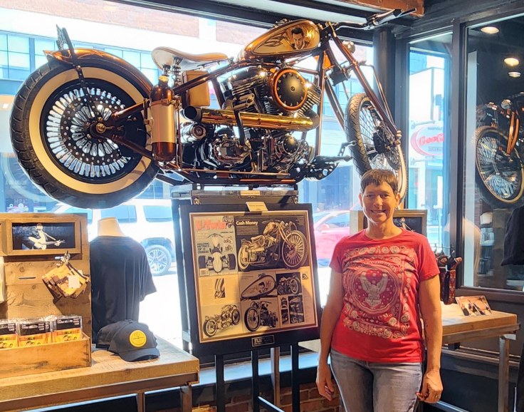 Wearing a red Harley-Davidson Motorcycle Museum shirt, the author stands in front of a Johnny Cash-themed custom bobber motorcycle named ‘Cash Money’ in the lobby of the Johnny Cash Museum.
