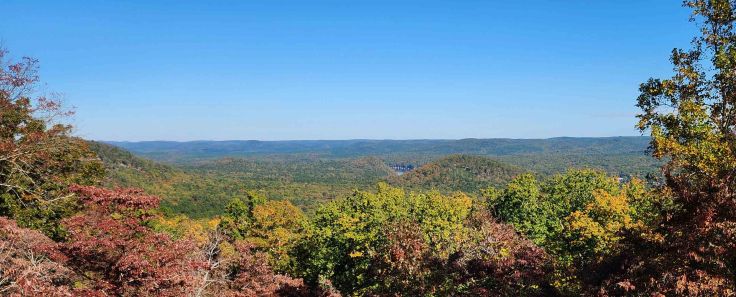 Sweeping mountain view of red, yellow, orange, and green foliage surrounding a small lake in distance.
