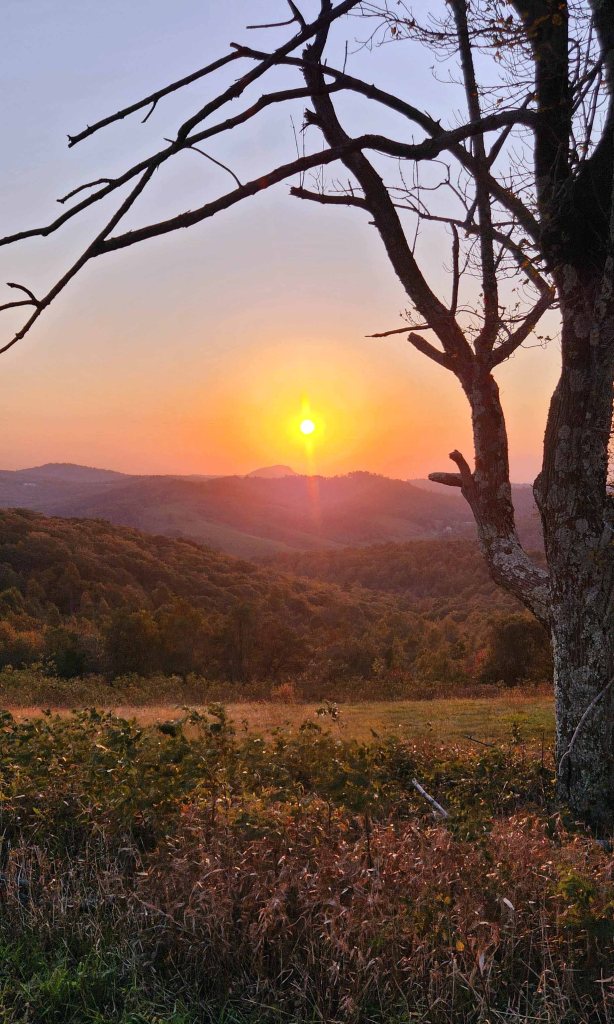 Bright orange sun setting behind Buffalo Mountain as viewed from The Saddle Overlook on the Blue Ridge Parkway in Virginia